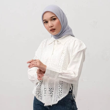 A woman wearing a white outer vest with lace details, paired with a hijab and jeans.