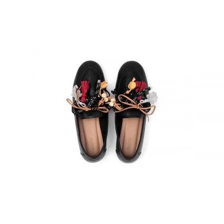 Black loafers flat shoes with colorful tassel decorations by Cajsa on a white background