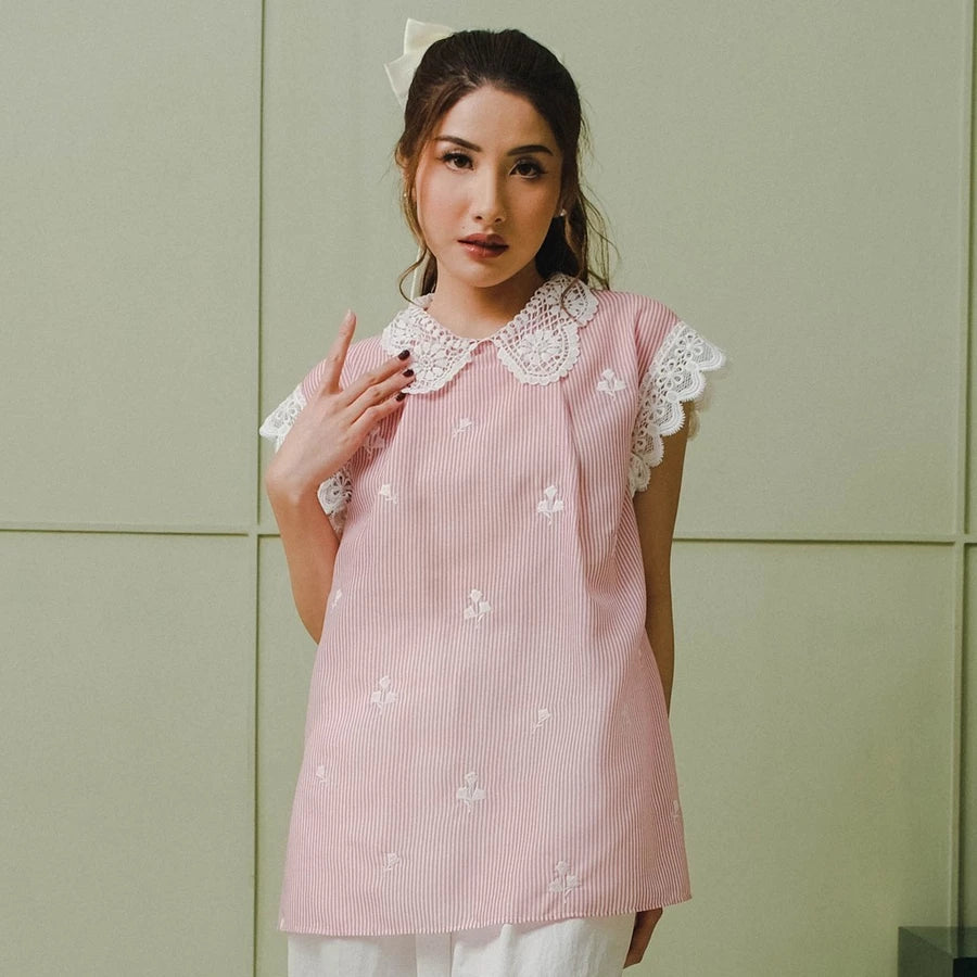 Woman wearing a pink embroidered blouse by Holy Peony with white collar against a light green wall