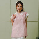Woman wearing a pink embroidered blouse by Holy Peony with white collar against a light green wall