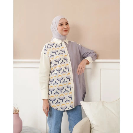 Woman wearing a patterned shirt by Abame in a room with a white wall and couch.