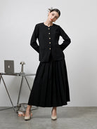 A model wearing a black Zora skirt by Kasa Heritage with pleats, paired with a matching brown top. The skirt reaches mid-calf and has a fitted waist with a zipper at the back.