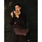 Woman in a brown outfit holding a burgundy woman's handbag by Prior against a building background.

Seorang wanita berpakaian cokelat memegang tas tangan wanita berwarna burgundy dari merek Prior di depan latar belakang bangunan.