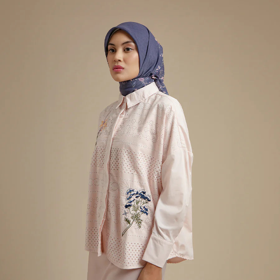 Woman wearing a light pink shirt by Hijabchic with floral embroidery and a blue hijab against a beige background