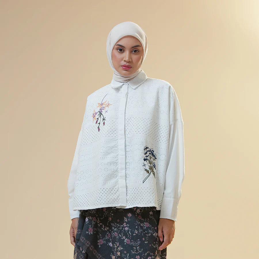 Woman wearing a white embroidered shirt by Hijabchic with floral patterns on a beige background